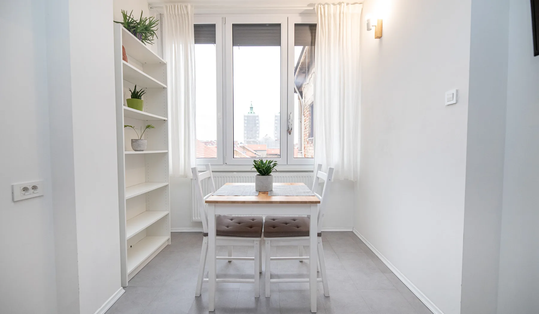 Dining table for two beside a tall window looking over Zagreb rooftops in the Woody 2 studio apartment